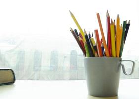 une tasse avec des crayons et une coin de le livre sur le table par le la fenêtre. flou Contexte. lieu de travail pour étude. photo