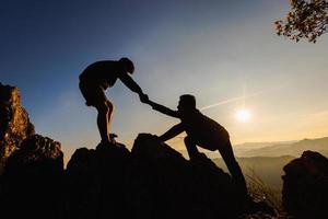 silhouettes de deux personnes grimpant sur la montagne et aidant. concept d'aide et d'assistance. photo