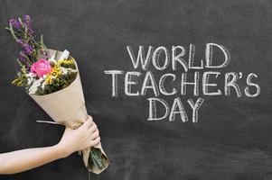 Gros plan main tenant un bouquet près du tableau de la journée mondiale des enseignants photo