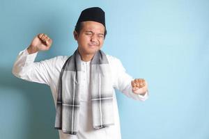portrait de attrayant asiatique musulman homme dans blanc chemise élongation le sien mains et corps après veille en haut. isolé image sur bleu Contexte photo
