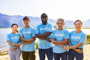 équipe de Jeune et la diversité bénévole ouvriers groupe prendre plaisir charitable social travail Extérieur dans plage nettoyage projet portant bleu T-shirt tandis que joindre main dans assembler unité concept photo