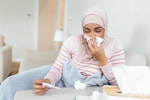 malade journée à maison. Jeune arabe femme a qui coule et commun froid. toux. fermer de magnifique Jeune femme avec hijab pris du froid ou grippe maladie. photo