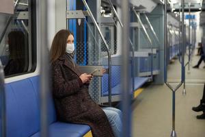 Une femme dans un masque facial est assise et à l'aide d'un smartphone dans une voiture de métro moderne