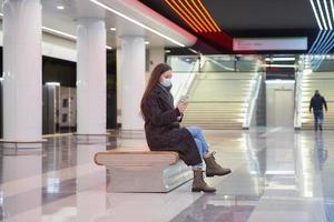 une femme dans un masque médical attend un train et tenant un smartphone photo