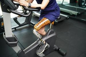 Jeune femelle avec un prothétique jambe avec exercice avec une filage bicyclette dans le Gym à entraine toi mixte utilisation avec le autre Ordinaire jambe à être flexible, concept de vivant une femme la vie avec une prothétique photo