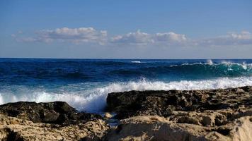 bleu mer vague et blanc mousse et éclaboussure. pierre plage sur île de Malte, non sablonneux plage. été vacances frontière Cadre concept. tropical île vacances toile de fond. touristique Voyage bannière conception modèle. photo