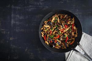 remuer frire avec poulet, aubergine et poivre dans wok la poêle sur foncé Contexte photo