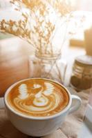 chaud latté art dans blanc tasse et sec fleurs décoration dans verre dans Naturel lumière du soleil à café photo