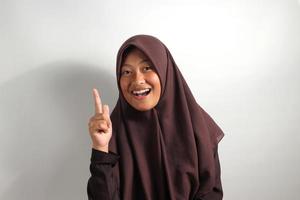 excité Jeune asiatique fille dans hijab montrer du doigt doigt la gauche sur blanc Contexte. photo