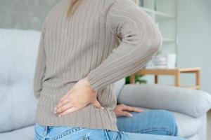 Asie magnifique femme en portant sa inférieur retour tandis que et souffrir de insupportable douleur santé et problèmes, chronique retour douleur, mal au dos dans Bureau syndrome, scoliose, hernie disque, muscle inflammation photo