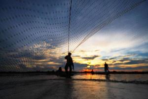 Silhouette de pêcheur sur bateau de pêche avec filet sur le lac au coucher du soleil, Thaïlande photo