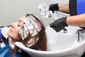 le coiffeur en gants noirs peint les cheveux d'une femme brune dans le salon de beauté. photo