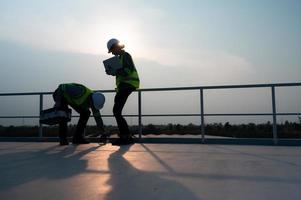 une équipe de électrique ingénieurs inspecter solaire panneaux dans une cent acres de herbe sur le toit de énergie espace de rangement gare, dans le soir après compléter le du quotidien travail Tâches avec le réglage Soleil photo