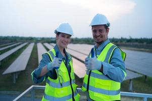 une équipe de électrique ingénieurs inspecter solaire panneaux dans une cent acres de herbe sur le toit de énergie espace de rangement gare, dans le soir après compléter le du quotidien travail Tâches avec le réglage Soleil photo