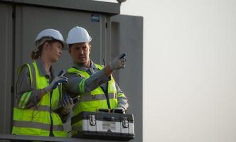 une équipe de électrique ingénieurs inspecter solaire panneaux dans une cent acre champ, dans le soir après compléter le du quotidien travail Tâches avec le réglage Soleil. photo