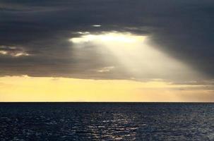 magnifique paysage vue de lumière du soleil brillant de le foncé des nuages à le mer ou océan à le coucher du soleil ou ensoleillement temps. beauté de la nature concept photo