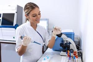 femme biologiste en utilisant micro pipette avec tester tube et gobelet pour expérience dans science laboratoire. biochimie spécialiste travail avec laboratoire équipement et verrerie pour développement. photo