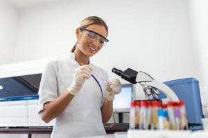 femme biologiste en utilisant micro pipette avec tester tube et gobelet pour expérience dans science laboratoire. biochimie spécialiste travail avec laboratoire équipement et verrerie pour développement. photo