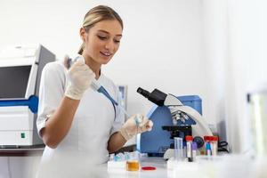 femme biologiste en utilisant micro pipette avec tester tube et gobelet pour expérience dans science laboratoire. biochimie spécialiste travail avec laboratoire équipement et verrerie pour développement. photo