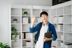 Masculin étudiant prise Remarques de une livre à bibliothèque, Jeune asiatique séance à bureau Faire affectations dans Université bibliothèque photo