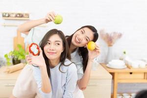 deux femmes asiatiques portant des vêtements de sport mangent des aliments sains dans la cuisine. jeune belle fille heureuse et aime manger des fruits des aliments sains. photo