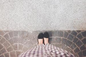 une femme des stands portant une paire de noir des chaussures sur une rue dans de face de une blanc pierre sol. photo