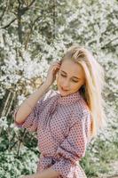 blond fille sur une printemps marcher dans le jardin avec Cerise fleurs. femelle portrait, fermer. une fille dans une rose polka point robe. photo