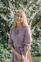 blond fille sur une printemps marcher dans le jardin avec Cerise fleurs. femelle portrait, fermer. une fille dans une rose polka point robe. photo