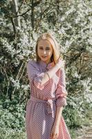 blond fille sur une printemps marcher dans le jardin avec Cerise fleurs. femelle portrait, fermer. une fille dans une rose polka point robe. photo