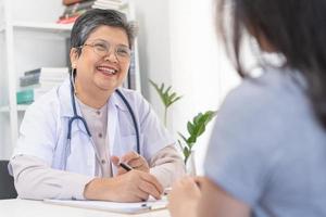 mature, Sénior asiatique médecin, psychiatre, général femme médecin consultant concerné avec Jeune patient, en utilisant stéthoscope à écouter, rendez-vous à clinique, hôpital. santé se soucier, vérifier en haut médical. photo