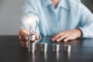 femme d'affaires main en portant ampoule avec empiler pièces de monnaie. idée de économie énergie et comptabilité la finance dans Accueil et famille, enregistrer monde et énergie pouvoir. enregistrer énergie plan concept photo