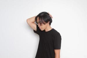 portrait de Beau asiatique homme dans noir T-shirt avec longue cheveux. modèle posant tandis que redressage cheveux avec main. isolé image sur blanc Contexte photo