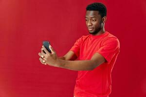 homme de africain apparence dans une rouge T-shirt avec une téléphone dans le sien mains isolé Contexte photo