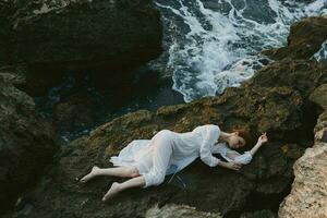 magnifique Jeune femme dans une isolé place sur une sauvage rocheux côte dans une blanc robe paysage photo