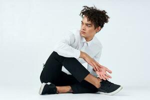 Jeune homme avec frisé cheveux est assis jambes croisées sur le sol photo