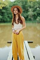 une Jeune femme dans une hippie Regardez et éco Vêtements voyages en plein air par le Lac portant une chapeau et Jaune un pantalon dans le tomber photo