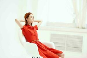 jolie femme dans rouge robe séance sur une chaise mode photo