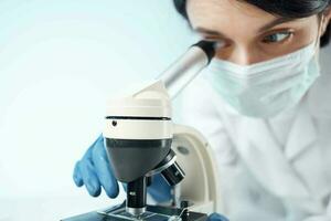 femme dans blanc manteau regards par microscope laboratoire science professionnels expérience photo