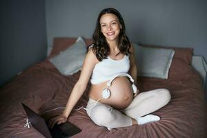 Enceinte femme avec écouteurs sur sa ventre à maison. photo