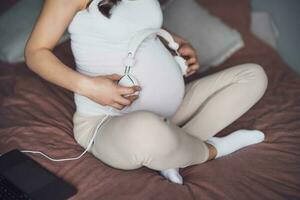 Enceinte femme avec écouteurs sur sa ventre à maison. photo