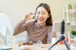 beauté concept, magnifique asiatique Jeune femme, fille maquillage visage par en utilisant un cil bigoudi à boucle mon cils avant appliquer mascara, à la recherche à le miroir à maison. femelle avec Naturel mode style. photo