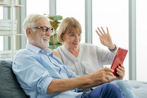 content mari et épouse Sénior couple personnes âgées famille, caucasiens mature, adulte amoureux et retraité homme, femme en utilisant tablette communicant, achats en ligne, en train de lire nouvelles sur canapé à Accueil ensemble. photo