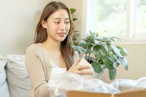 content asiatique Jeune femme, client reçu, déballer paquet carton ouvert parcelle dans papier carton boîte, en portant céramique plante pot. en mouvement, en train de préparer dans Nouveau loger, déménagement. en ligne magasin livraison à maison. photo