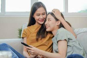 content lesbienne, plaisir asiatique Jeune deux femmes, fille gay ou proche ami, couple l'amour en utilisant éloigné contrôle en train de regarder la télé, moment dépenses bien temps ensemble sur canapé à maison. activité de loisirs, se détendre. photo