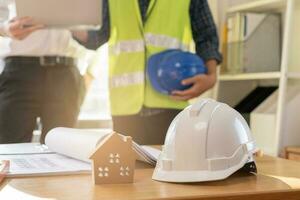 proche en haut blanc sécurité difficile casque. asiatique, caucasien Jeune ingénieur, architecte deux homme sont discuter construction à suivre le projet à construire un industriel plan à placer. ingénieur ouvrier personnes. photo