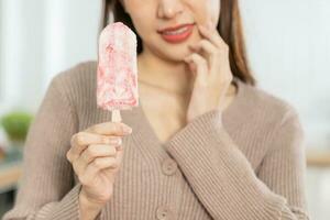 santé asiatique Jeune femme émouvant joue, expression, Souffrance de mal aux dents, pourriture ou sensibilité cavité molaire dent, les dents ou inflammation manger du froid la glace crème à maison. sensible les dents personnes. photo