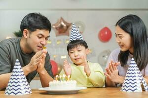 content anniversaire fête dans famille, asiatique Jeune parent père, mère et peu mignonne garçon ou enfant célébrer, soufflant bougies sur le gâteau et décoré des ballons, fête à maison. charmant des moments photo