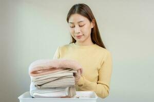 corvée de femme au foyer, sourire asiatique Jeune femme pliant beaucoup fraîchement chemises mettre le tissu dans le panier après la lessive nettoyer vêtements et séchage, fabrication Ménage travail dans pièce à maison, Femme de ménage blanchisserie rangé. photo