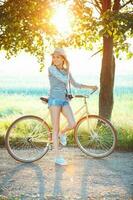 charmant Jeune femme dans une chapeau équitation une vélo dans une parc photo