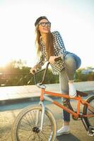 charmant Jeune femme dans une chapeau équitation une vélo sur ville Contexte dans le lumière du soleil Extérieur photo